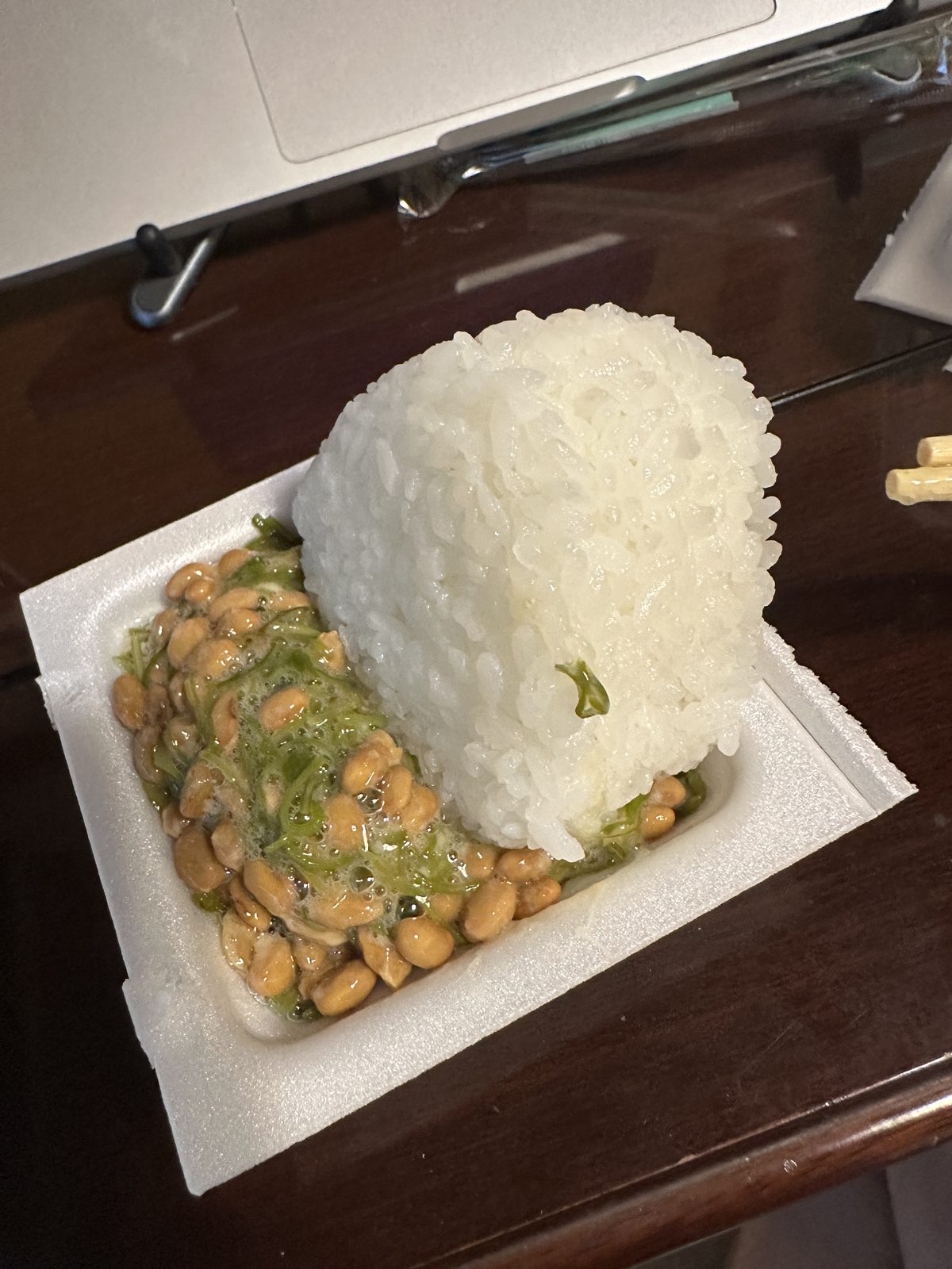 2食目（08:48）。 塩むすび1個を、糸挽き納豆とめかぶを混ぜたパックの上に載せたところ。納豆・めかぶはこの日2パック目。